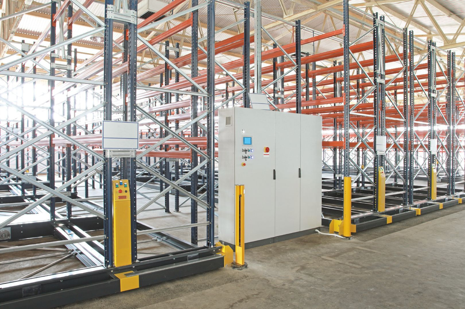 Automatisches Palettenregal mit Steuerschrank, Bodenschienen und gelben Sicherheitspfosten, in Industriehalle installiert