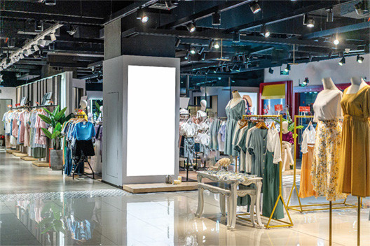 Moderne Ladenfläche mit Kleidung, Mannequins und beleuchteter Digitalanzeige für flexible Storegestaltung.