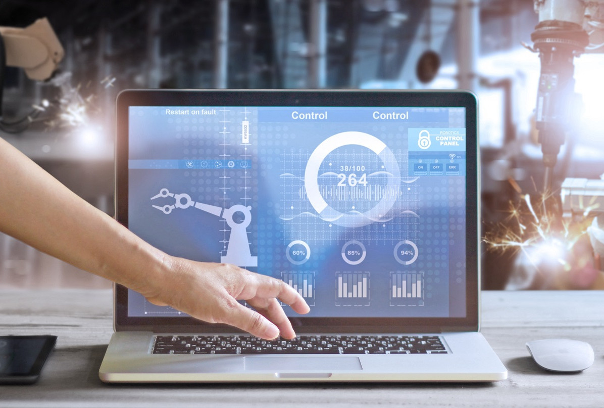 Hand operating laptop with industrial control dashboard monitoring robotic machinery and cybersecurity.