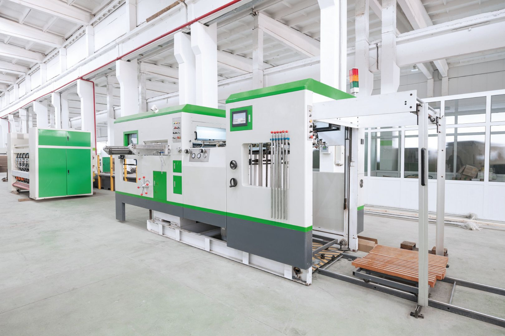 Automatisierte Produktionsmaschine mit Förderbereich, grüner Verkleidung und Bedienpanel in moderner Fabrikhalle.